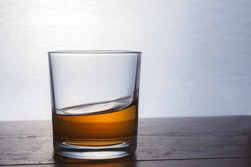 A glass of whiskey stands on a wooden table in backlight