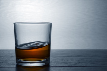 A glass of whiskey stands on a wooden table in backlight