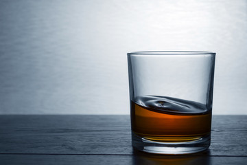 A glass of whiskey stands on a wooden table in backlight