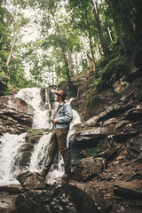 Stylish young man in hat traveling in mountains. Hipster man with photo camera exploring  beautiful...