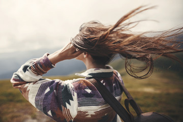 Stylish hipster girl with backpack  and windy hair on top of mountains. Portrait of happy young...