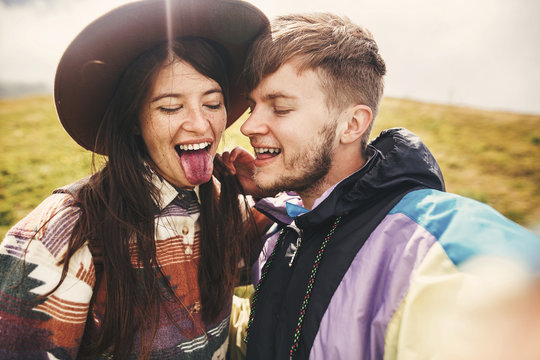 Happy hipster couple making selfie and showing tongue on top of  sunny  mountains. Stylish couple in love taking selfie photo and having fun. Travel together and Wanderlust concept.