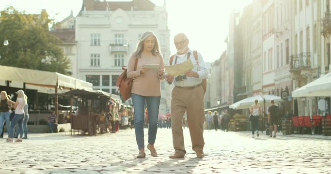 Caucasian tourist couple walking the city center square with a map and tablet device on a nice sunny day. Outside.