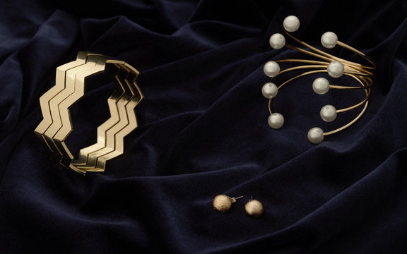 Golden modern Bracelets and pair of earrings on dark blue velvet fabric
