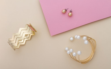 Golden and pearls bracelet and golden cuff with pair of earrings on pink and beige