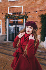 Fototapeta premium A beautiful girl in a red coat and a beret is walking along the Christmas street.