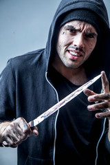 Hooligan young man in hood with a knife as symbol of aggression and deviant behaviors. Crime...