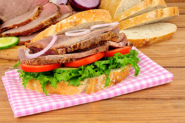 Roast beef and salad sandwich with ingredients on a wood background