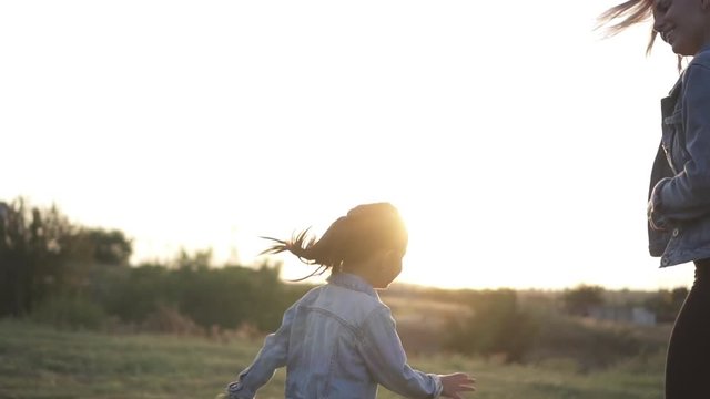 Little chinese girl runs around and try to catch her mother in park. Mixed race family, european mother and asian doughter, spending time in the park on sunset. Warm spring or summer season