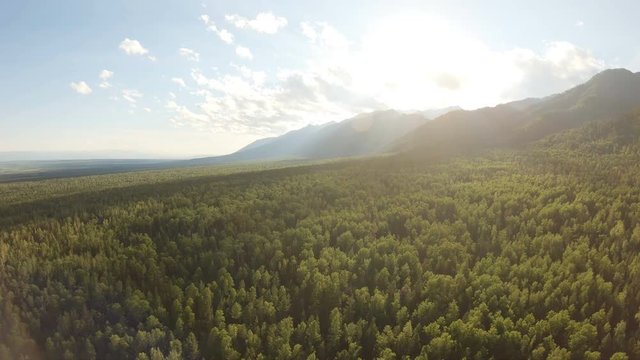 Aerial shot of beautiful landscape: mountains, forest, blue sky with clouds, sunset. Drone flying down above the treetops