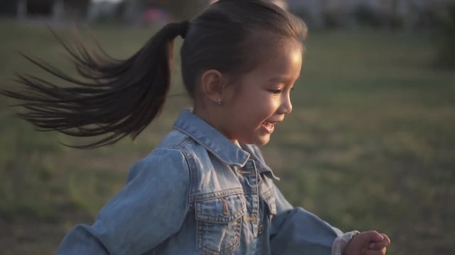 Cute little asian girl running around in the park going to her mother. Mixed race family, european mother and chinese doughter, spending time in the park on sunset. Warm spring or summer season.