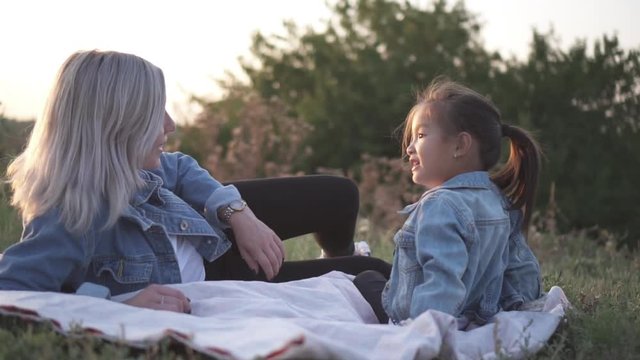 Mixed race family, european mother and asian daughter spending time in the park on sunset tolking and smiling. Warm spring or summer season