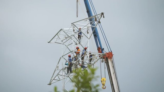 Linesmen worker working at height on transmission pylon lattice tower. 4k establishing cinematic shot. 