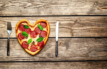 Heart shaped pizza on vintage wooden table background. The concept of romantic love for Valentine's Day