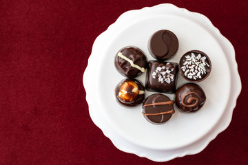 Assorted fancy chocolate candy on a white cake stand on a red background for Valentine’s Day