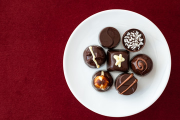 Assorted fancy chocolate candy on a white plate on a red background for Valentine’s Day