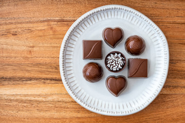 Assorted milk and dark chocolate candy on a rustic white plate on a wood background for Valentine’s Day