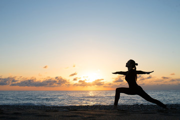 silhouette of woman doing yoga on the beach at sunrise