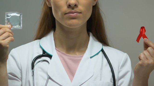 Female physician holding condom and red ribbon, safe sex concept, HIV prevention