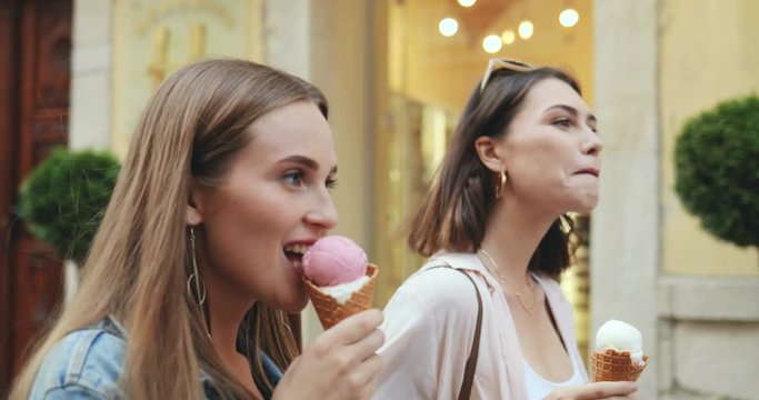 Close up of the two young pretty Caucasian women walking the street and eating ice-cream. Outdoor.