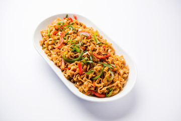 Schezwan veg noodles is a spicy and tasty stir fried flat Hakka noodles with sauce and veggies. served with chopsticks. selective focus