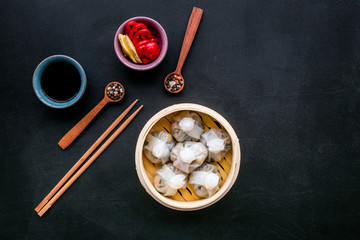 Chinese steamed dumplings Dim Sum with sweet paper and spices in bamboo steamer on black background top view
