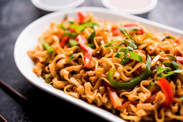 Schezwan veg noodles is a spicy and tasty stir fried flat Hakka noodles with sauce and veggies. served with chopsticks. selective focus