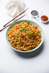 Schezwan veg noodles is a spicy and tasty stir fried flat Hakka noodles with sauce and veggies. served with chopsticks. selective focus