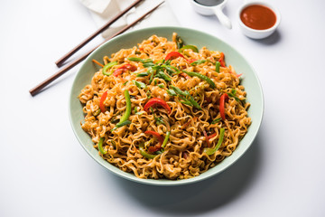 Schezwan veg noodles is a spicy and tasty stir fried flat Hakka noodles with sauce and veggies. served with chopsticks. selective focus