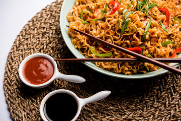 Schezwan veg noodles is a spicy and tasty stir fried flat Hakka noodles with sauce and veggies. served with chopsticks. selective focus