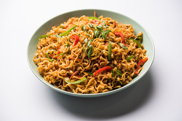 Schezwan veg noodles is a spicy and tasty stir fried flat Hakka noodles with sauce and veggies. served with chopsticks. selective focus