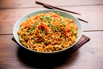 Schezwan veg noodles is a spicy and tasty stir fried flat Hakka noodles with sauce and veggies. served with chopsticks. selective focus