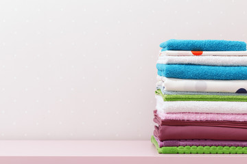 On the dresser there is a stack of clean ironed bed linen and folded colored towels.