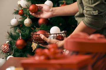 handsome man decorating christmas tree with baubles and looking at camera at hom