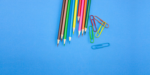 Art and drawing concepts, Colored crayon pencils and clips at top corner on blue background with copy space. Wide web banner, poster, brochure template design. Top view, Closeup.