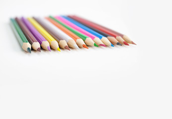 Assorts colorful crayon pencils in row on white background with selective focus on the tip of pencils in the middle on white background. Closeup.