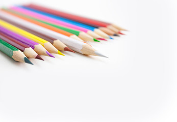 Colored crayon pencils in a row on the white desktop with selective focus on the white color tips with copy space. View from above.