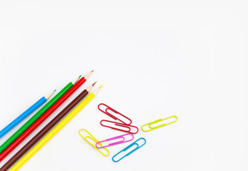 Office utensils supplies concepts, Colorful crayon pencils and multi-colored clips on white background with copy space. View from above.