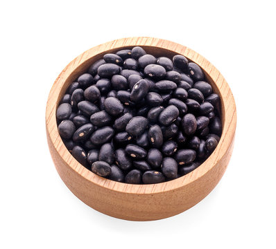 Dry black beans in dark wooden bowl isolated on white
