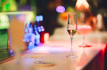 Champagne glass drink-beverage on  a bar.  Selective focus on the foreground glass,night background . Blurred people in the background.  Trendy black stylish  edit. Copy paste space for design concept
