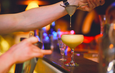 Cocktail being poured at a bar preparing a drink. Motion blur of the bartender's hand and strainer. Selective focus on the foreground glass. Blurred people in the background.  Trendy black stylish 