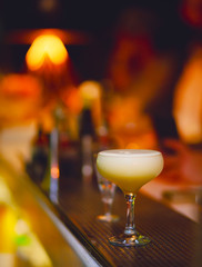 White Cocktail drink-beverage on  a bar.  Selective focus on the foreground glass,night background . Blurred people in the background.  Trendy black stylish  edit. Copy paste space for design concept