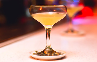 Cocktail being on bar drink on a stand . Selective focus on the foreground glass. Blurred people in the background.  Trendy black stylish alcohol nightlife  edit 