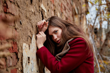 Girl in a red coat near the red brick wall in the Park in late autumn