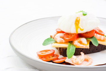 Ready-to-eat sandwich on rye bread with poached egg, tomato, shrimp and arugula on a plate