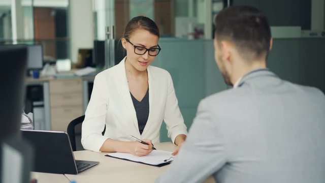 Pretty woman recruiter is talking to male candidate during job interviewer in office, girl is taking notes then shaking his hand and laughing. Success and workplace concept.
