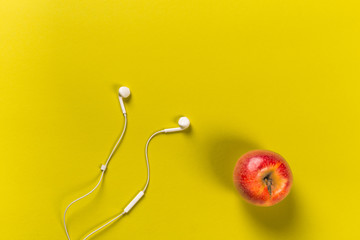 single red color apple and digital audio headphones on yellow background, top view
