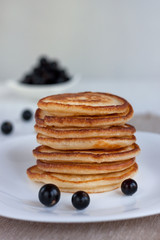 Stack of american pancakes and fresh blackcurrant are lying on a white plate.