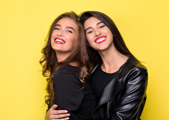 Two beautiful girls hugging on yellow background