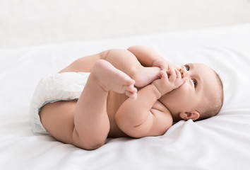 Adorable little baby sucking foot lying on bed